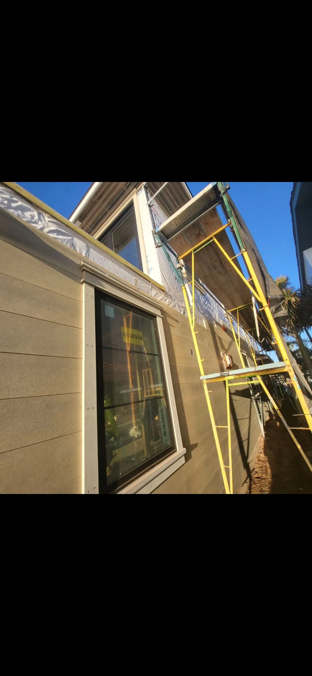 Exterior wall with horizontal siding installation in progress, scaffolding, and window trim